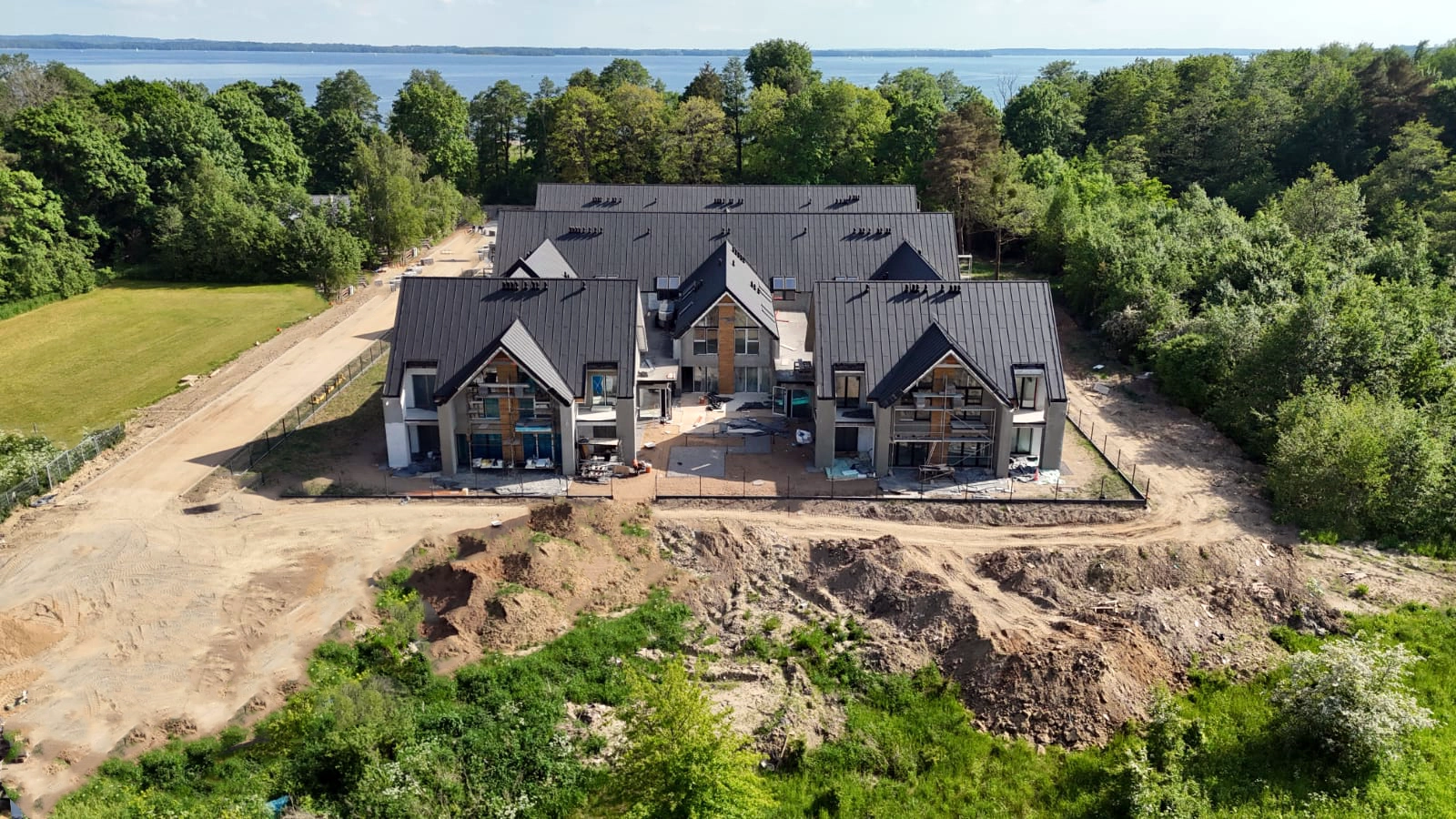 Widok z drona na linię brzegową jeziora oraz zielone tereny wokół Yacht Apartment
