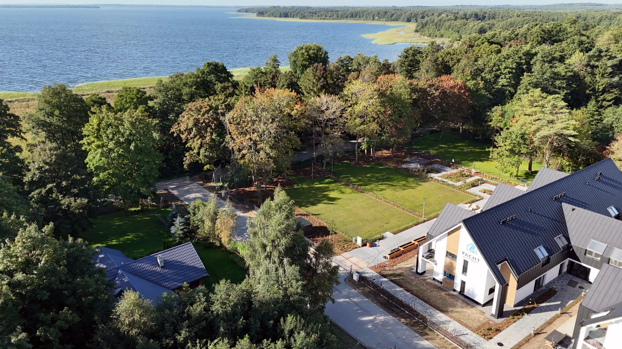 Kompleks Yacht Apartment widziany z drona wśród zieleni, z rozległym jeziorem w tle
