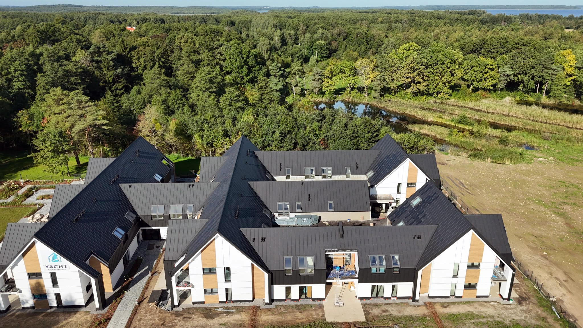 Front budynków Yacht Apartment widziany z drona z lasem i zielonym terenem wokół kompleksu