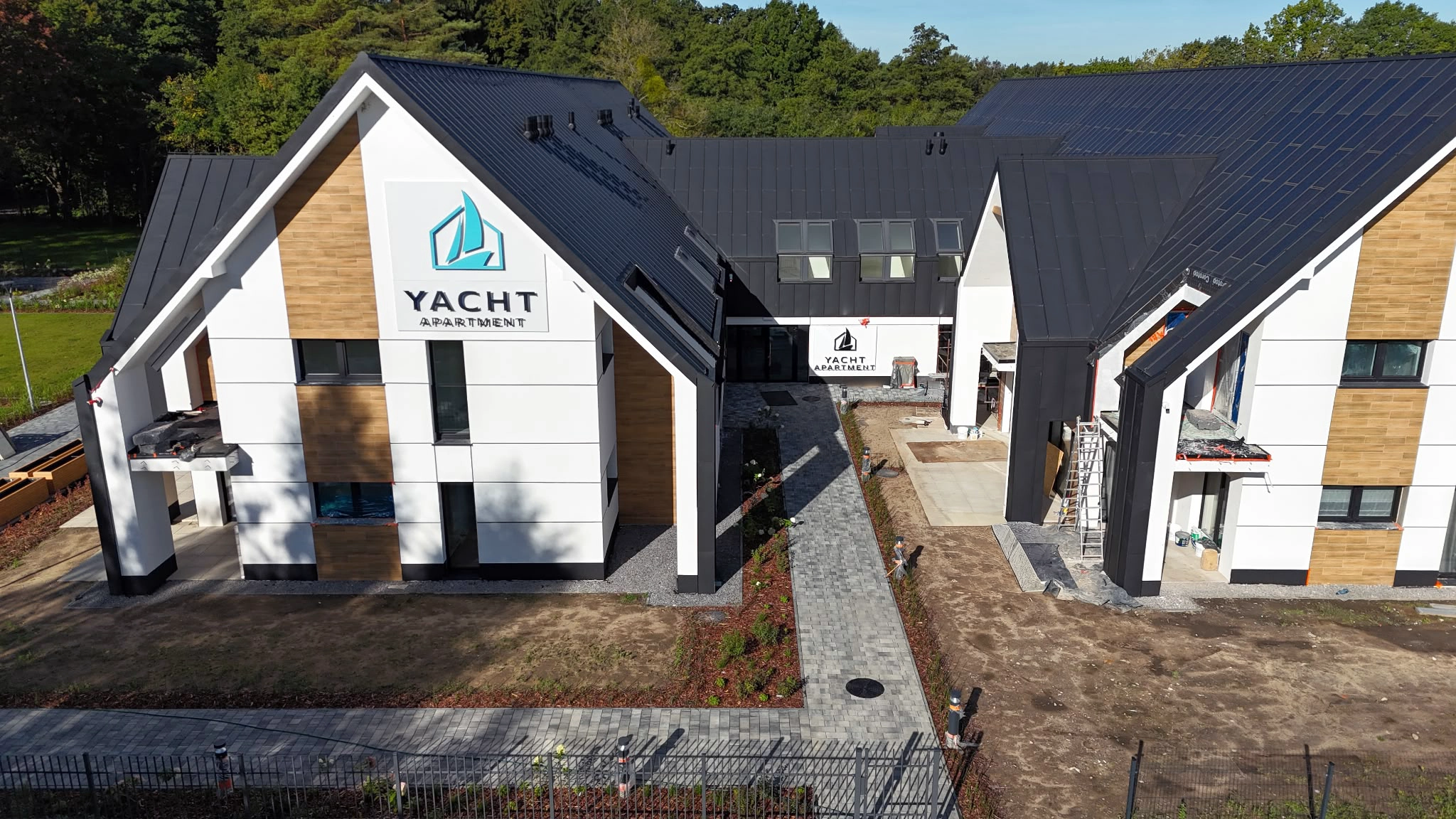 Elewacja Yacht Apartment z logo marki, drewnianymi akcentami i przejściem pomiędzy budynkami